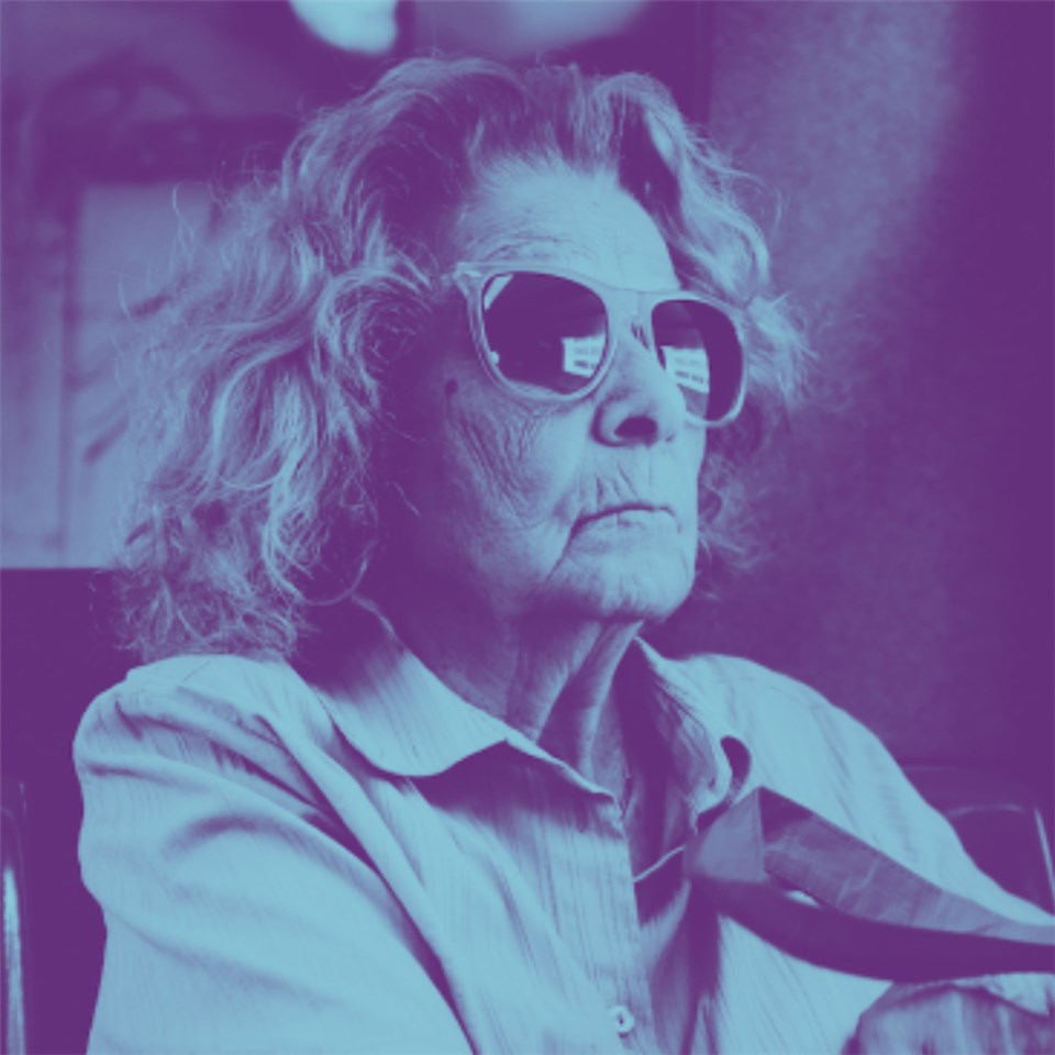 Eine alte Frau trägt eine große Sonnenbrille. Das Bild ist blau unterlegt. 