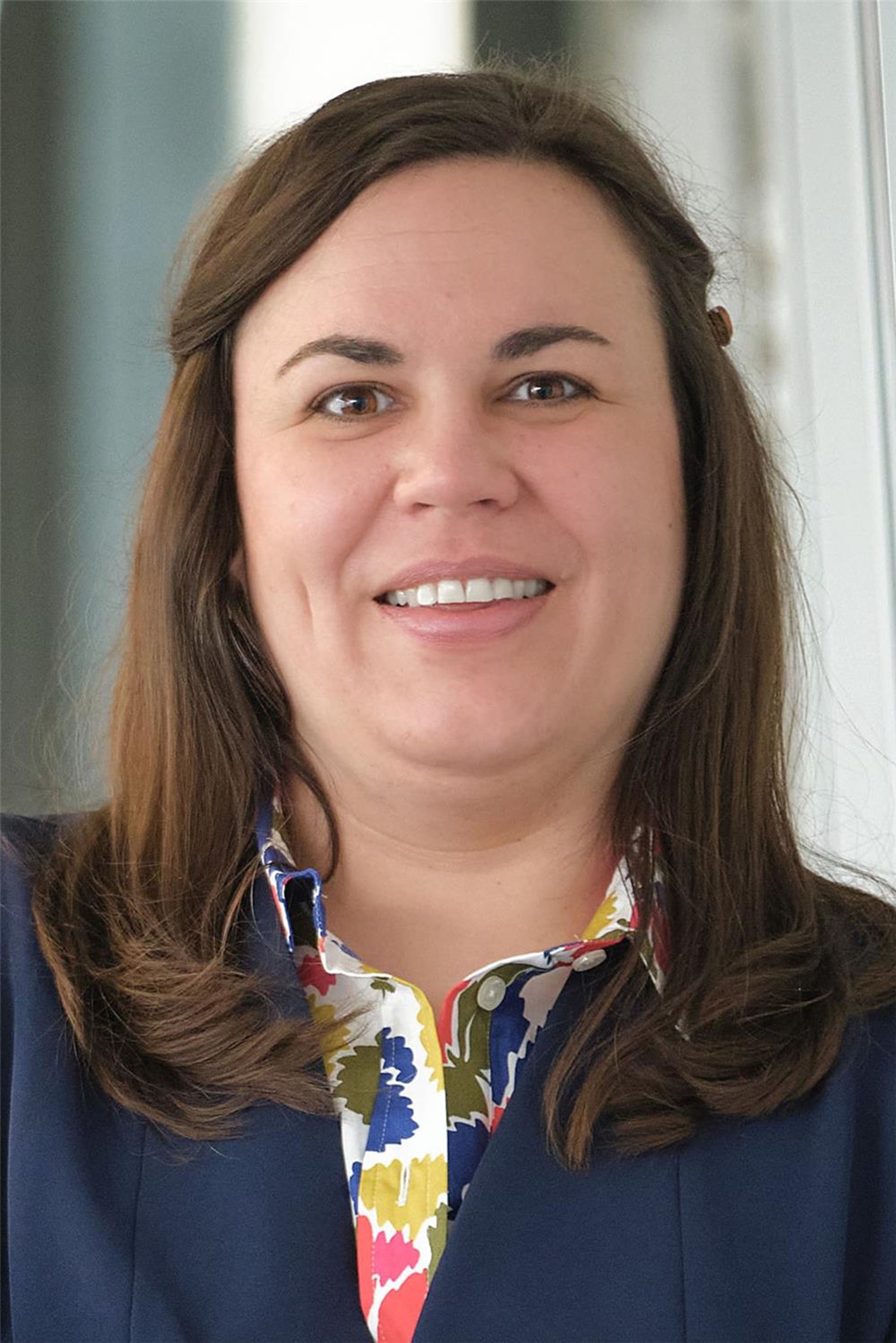 Porträt: Dr. Marie Kajewski mit schulterlangem braunem Haar lächelt in die Kamera. Sie trägt eine bunte Bluse und einen blauen Blazer.